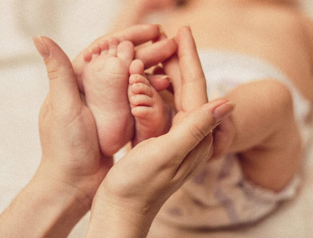 Hebamme Frauenhände halten die Füße von einem Neugeborenen Baby in der Hand