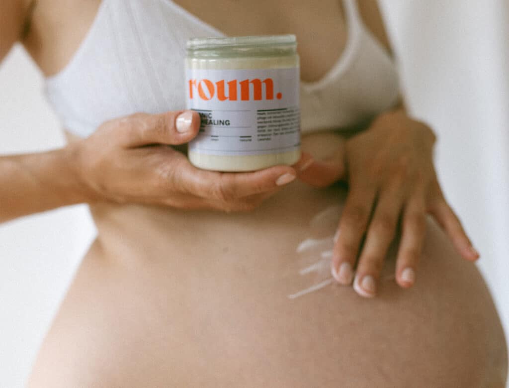 Schwangere Frau die nur mit einem BH bekleidet Ihren Bauch mit der Belly Mask einreibt und Pflegt.
