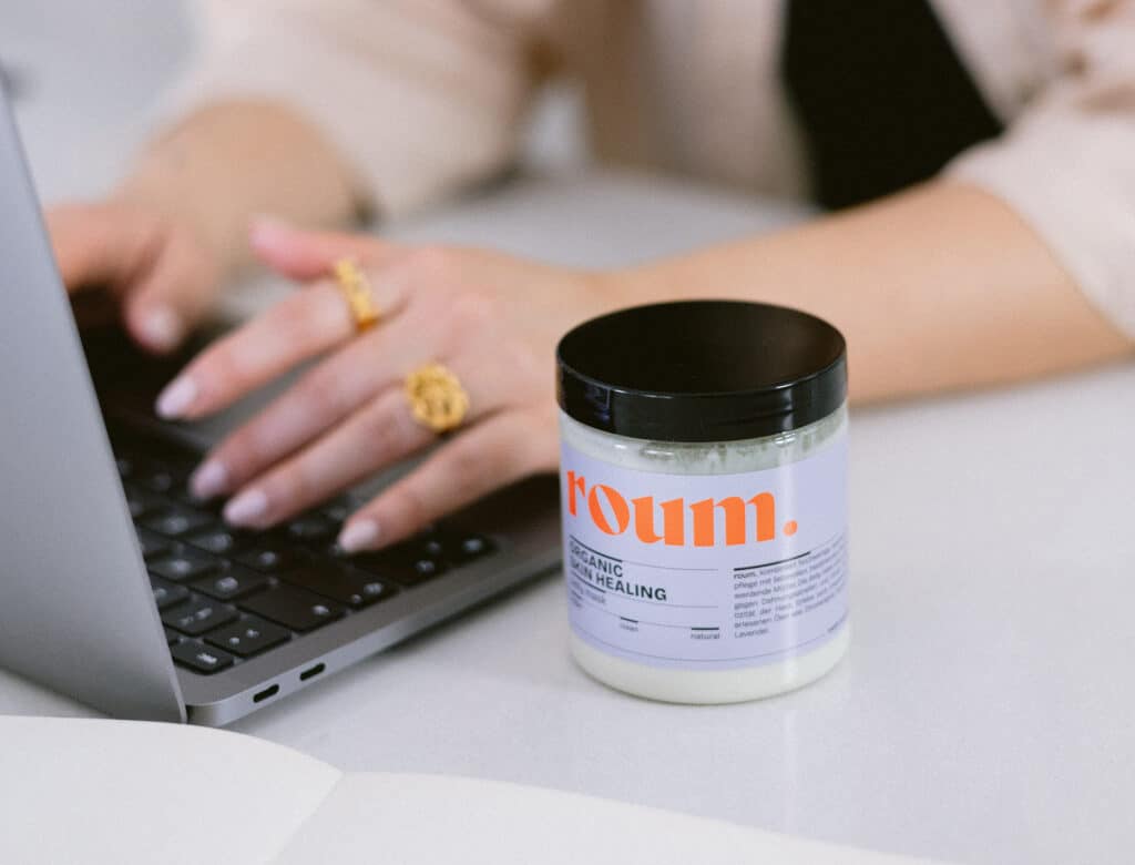 Frau arbeitet am Laoptop und nben dem Laptop steht eine roum bellymask Creme Dose.